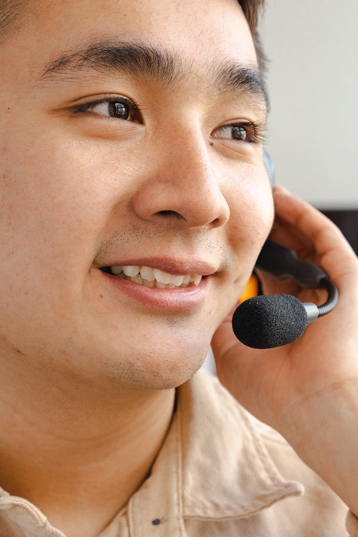 Close-up of a smiling Asian man working as a call center agent with a headset in an indoor setting.